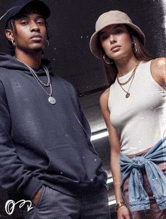 Two stylish individuals, one in a hoodie and cap, the other in a hat and tank top, pose confidently in casual urban attire.