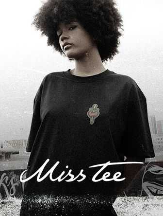 Person with curly hair wearing a black T-shirt with a small design, standing outdoors with an urban backdrop. Text reads "Miss tee."