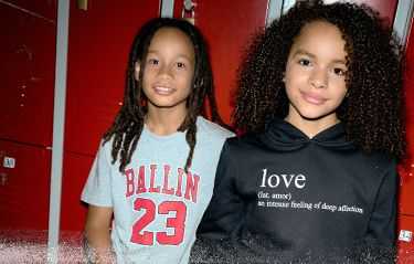 Two kids standing in front of red lockers, one in a "Ballin 23" shirt, and the other in a hoodie with "love" definition.