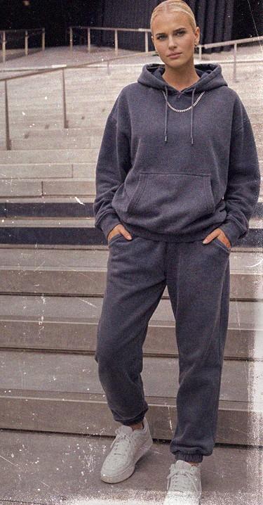 Person in a gray hoodie and sweatpants stands on steps, hands in pockets, wearing white sneakers.