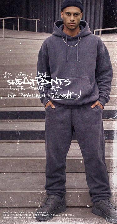 Person wearing a dark tracksuit and sneakers stands confidently on steps, with graffiti-style text overlayed in the background.