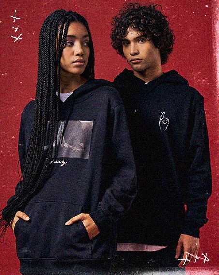 Two individuals wearing black hoodies stand against a red background, showcasing casual fashion with graphic designs.