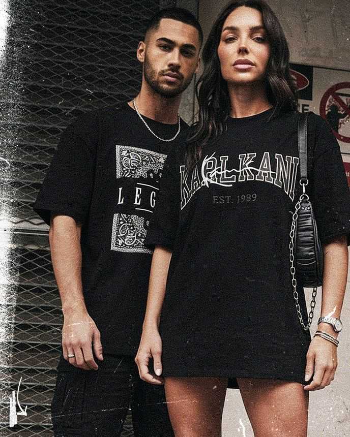 A man and woman in black shirts pose confidently in front of a metal grate. The woman's shirt reads "Karl Kani EST. 1989."