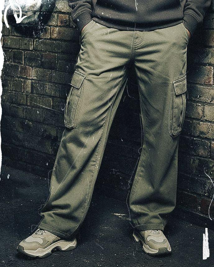 Person wearing green cargo pants and sneakers, standing against a brick wall with hands in pockets.