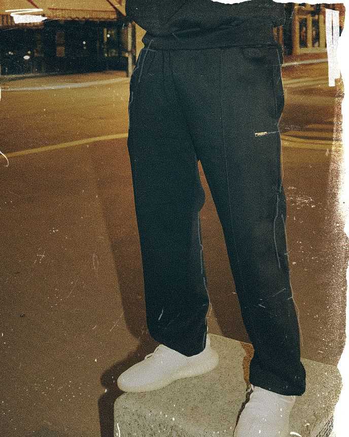 Person wearing black pants and white shoes stands on a concrete block in a dimly lit urban street setting.