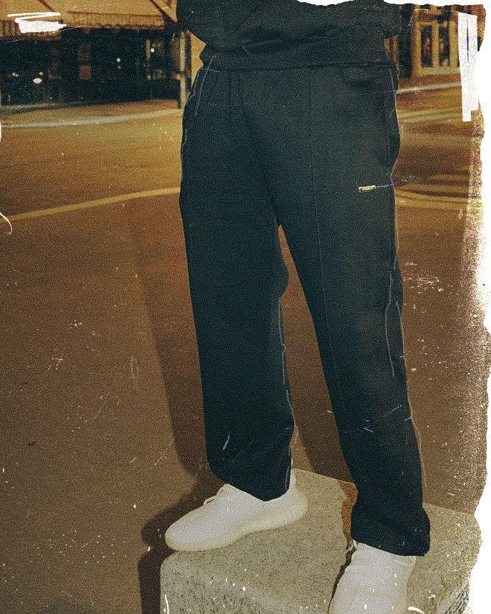 Person wearing black pants and white shoes stands on a concrete block in a dimly lit urban street setting.