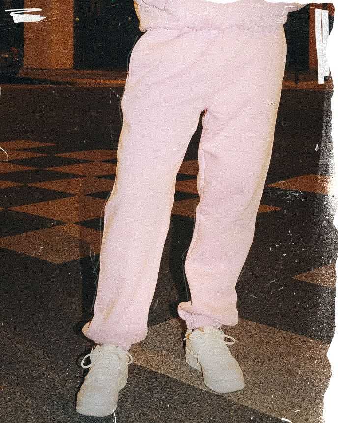 A person wearing pink sweatpants and white sneakers stands on a checkered floor, partially visible in a dimly lit area.
