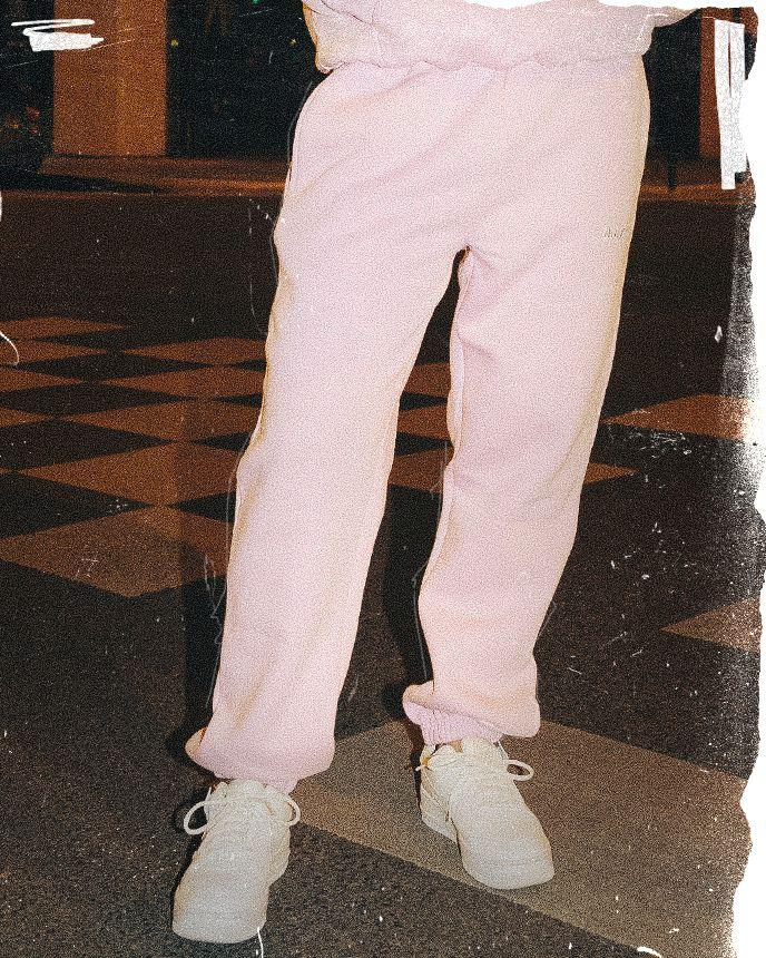 A person wearing pink sweatpants and white sneakers stands on a checkered floor, partially visible in a dimly lit area.