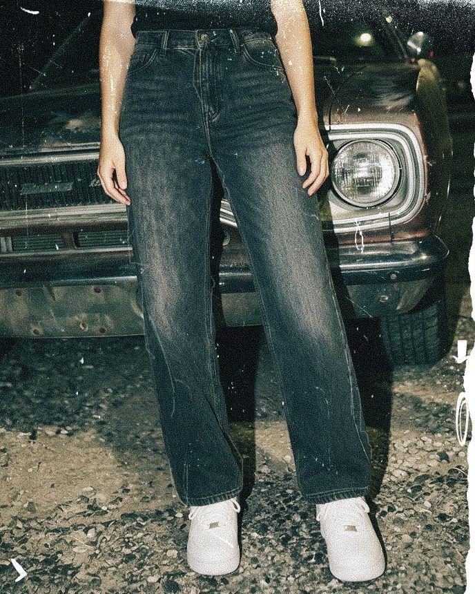 Person in black jeans and white sneakers standing in front of an old car with a visible headlight.