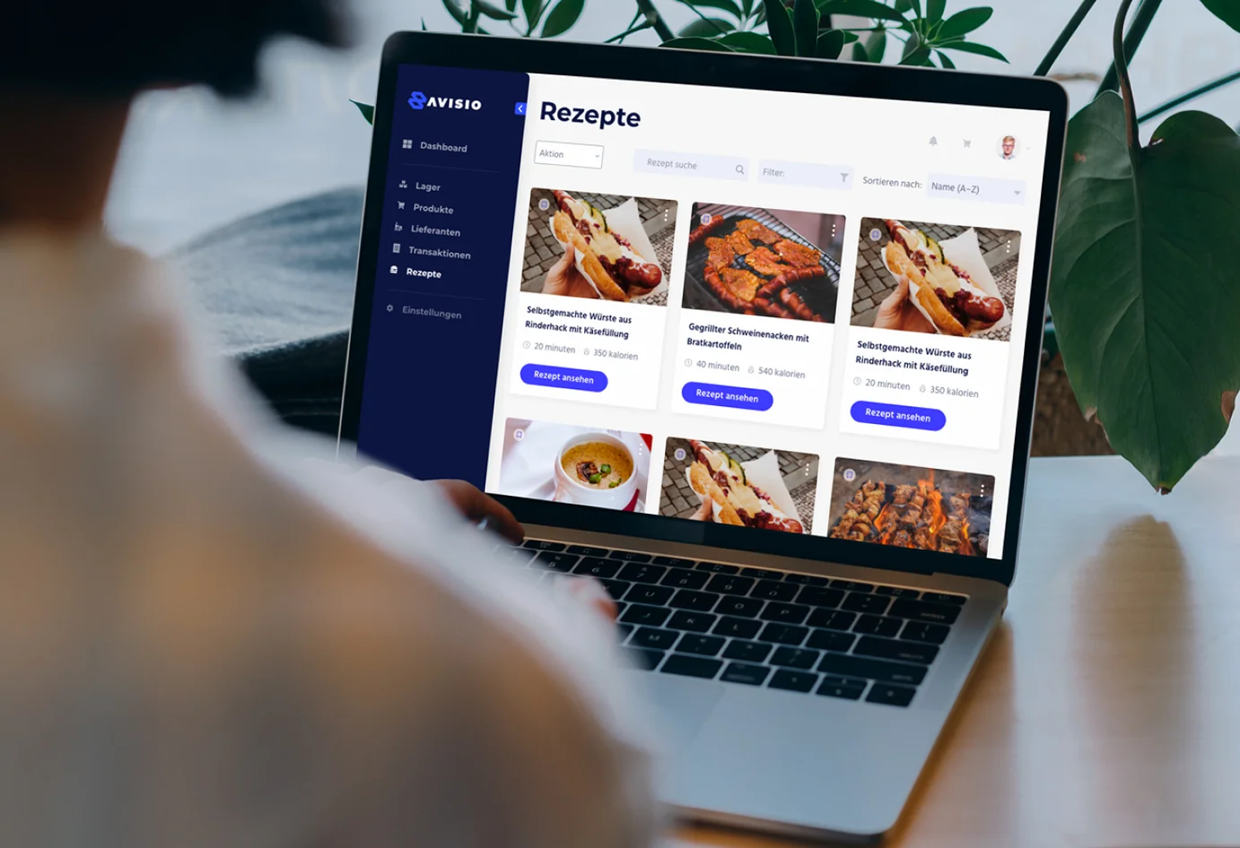 Picture of a laptop on a desk with a plant in the background and a person's back in the foreground. On the laptop screen there is a view from the Avisio hotel inventory management application built by Monterail.