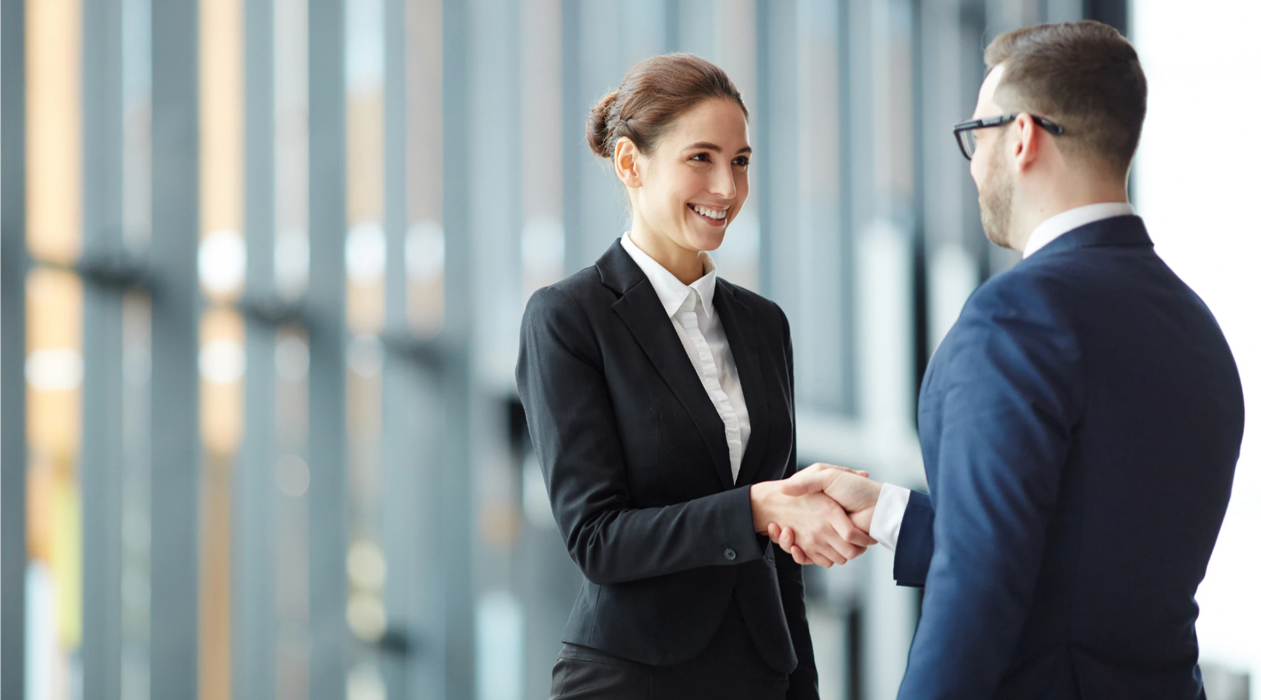 Picture of sharply dressed woman and man shaking heads on a blurry background.