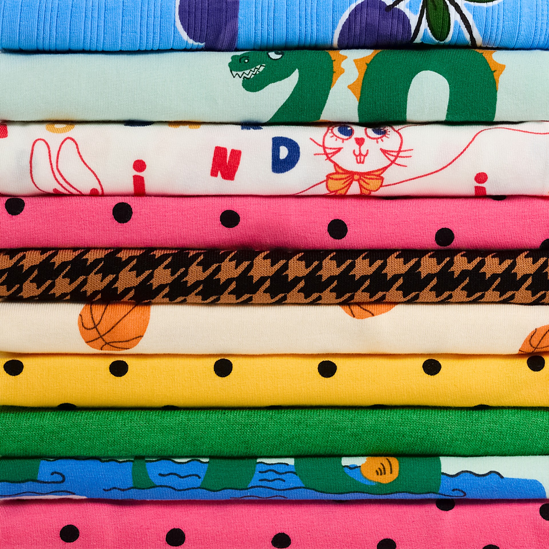 Stack of colorful fabric pieces with various patterns, including stripes, polka dots, loch ness, and rabbit, from Mini Rodini Upcycling collection.