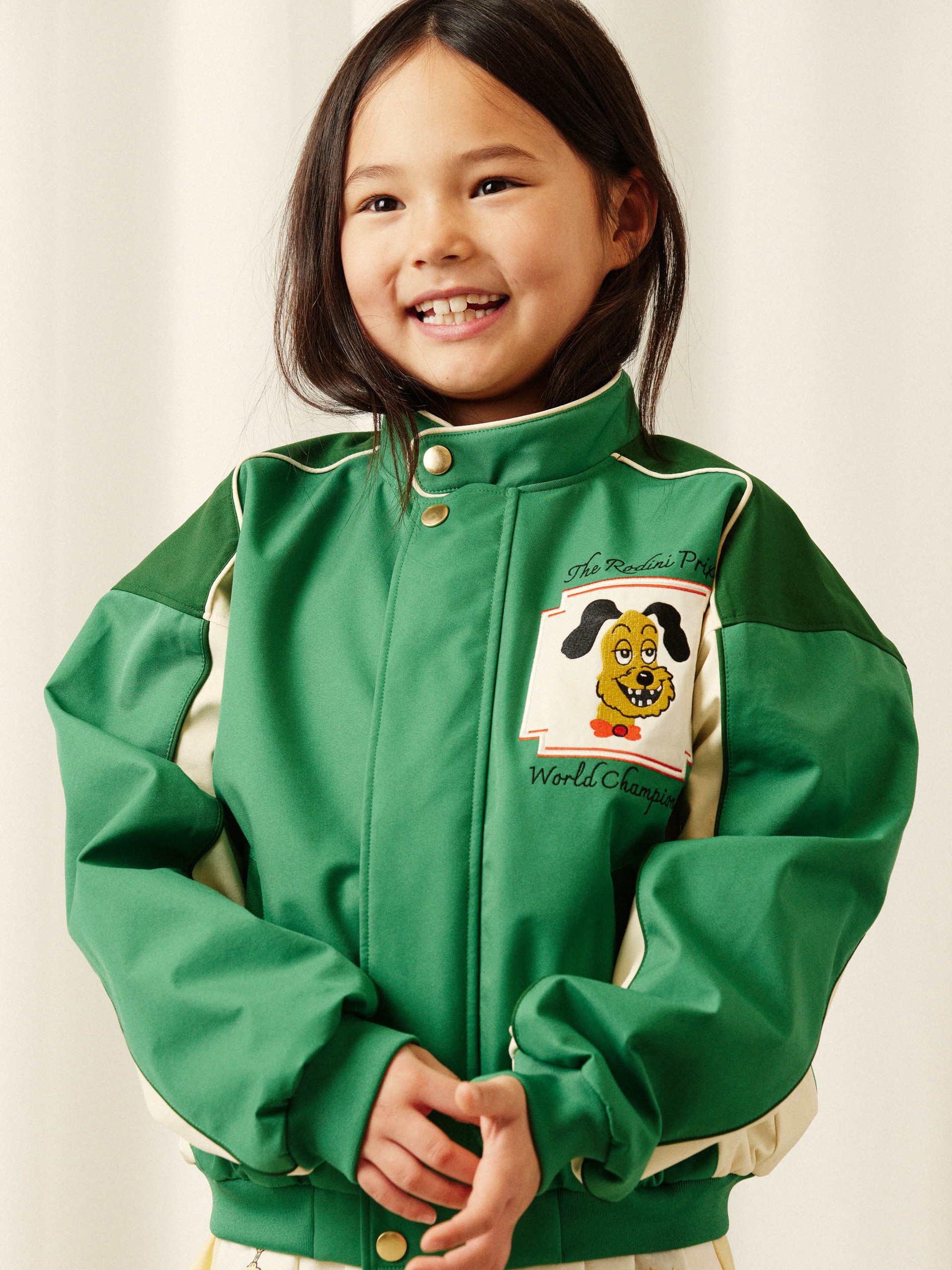 A smiling child wearing a green jacket with cartoon dog patch and text "World Champion."