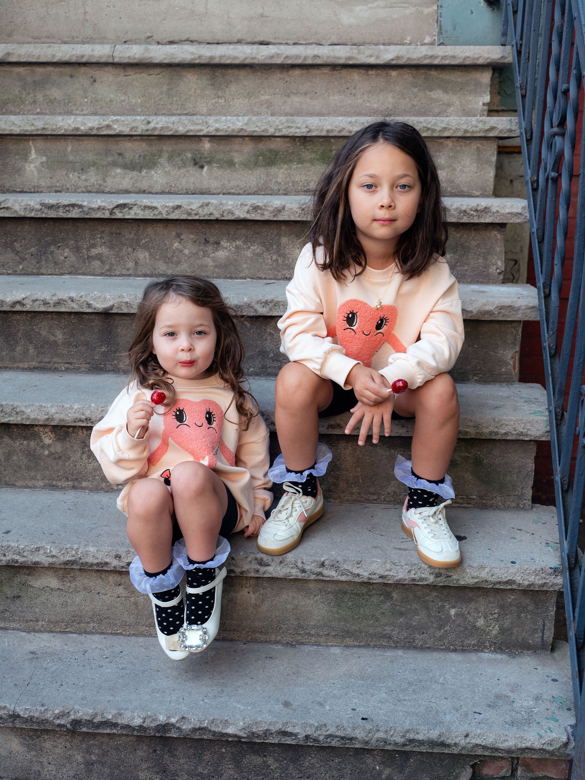 Two girls sitting on stairs wearing Heart in shoe Sweatshirt from Mini Rodini Things to love collection