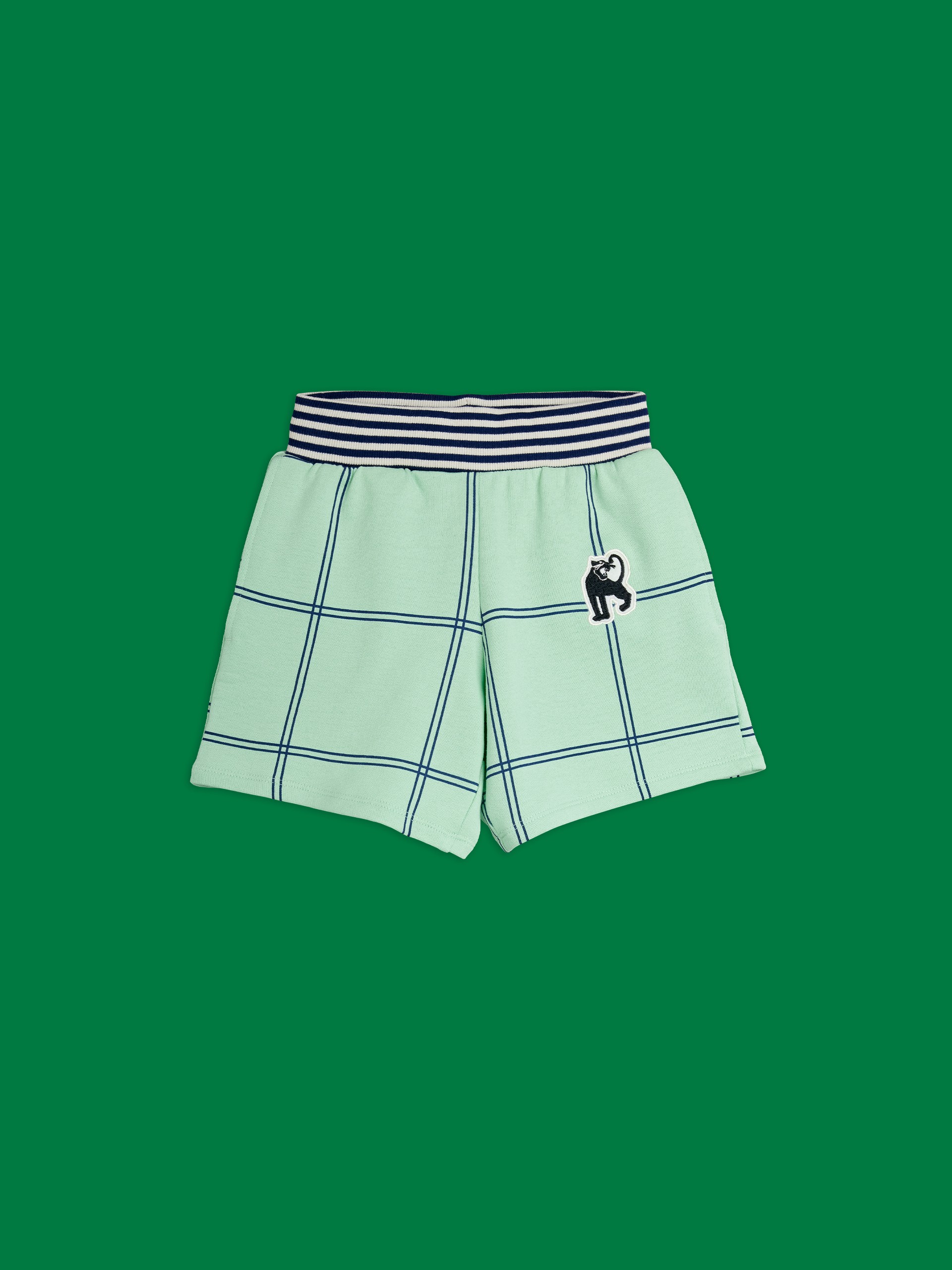 Check panther patch Sweatshorts from Mini rodini with a black cat patch and striped waistband, set against a solid green background.