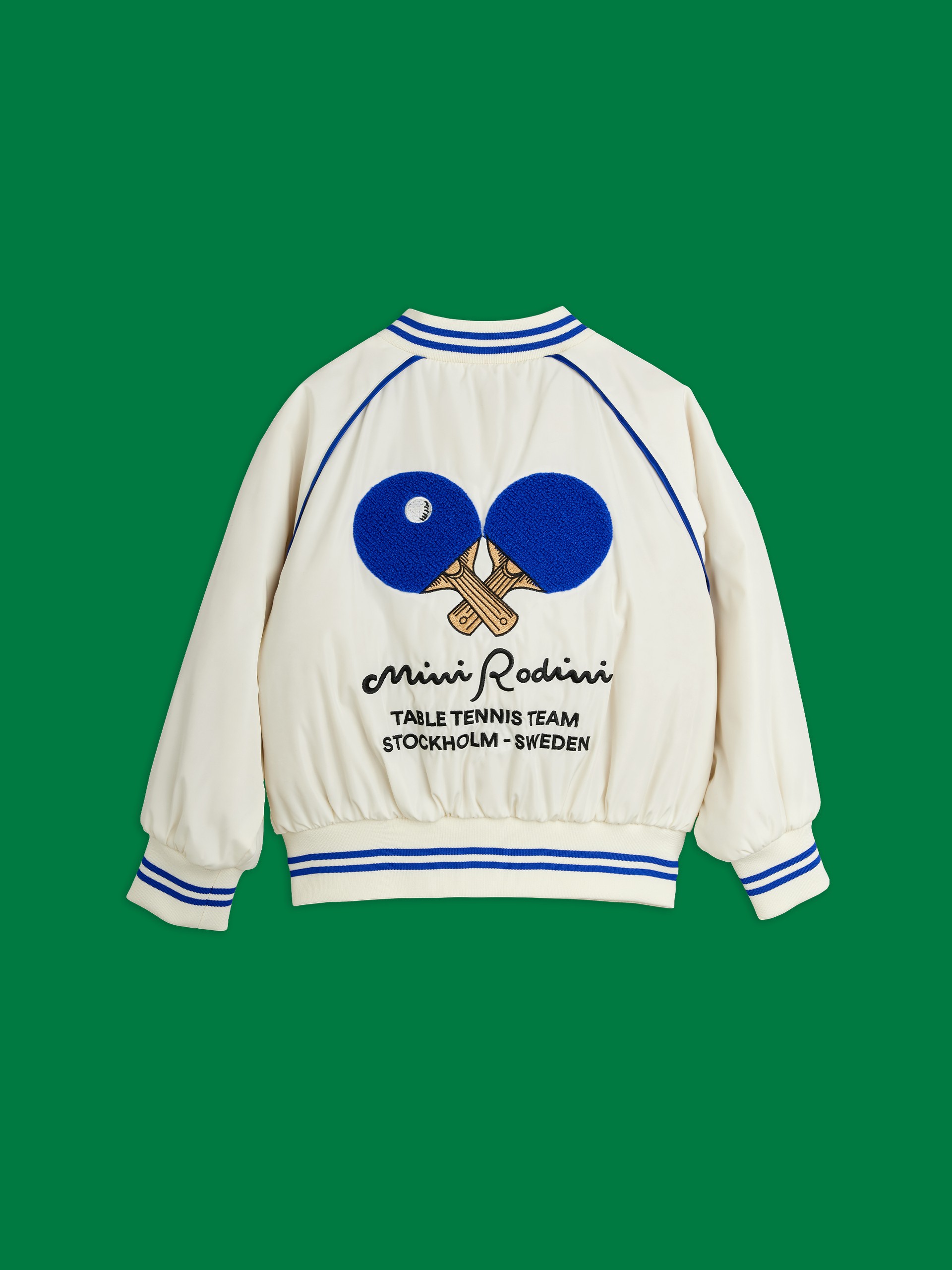 White jacket with blue-striped cuffs and collar, featuring table tennis paddles and text "Mini Rodini Table Tennis Team, Stockholm - Sweden."