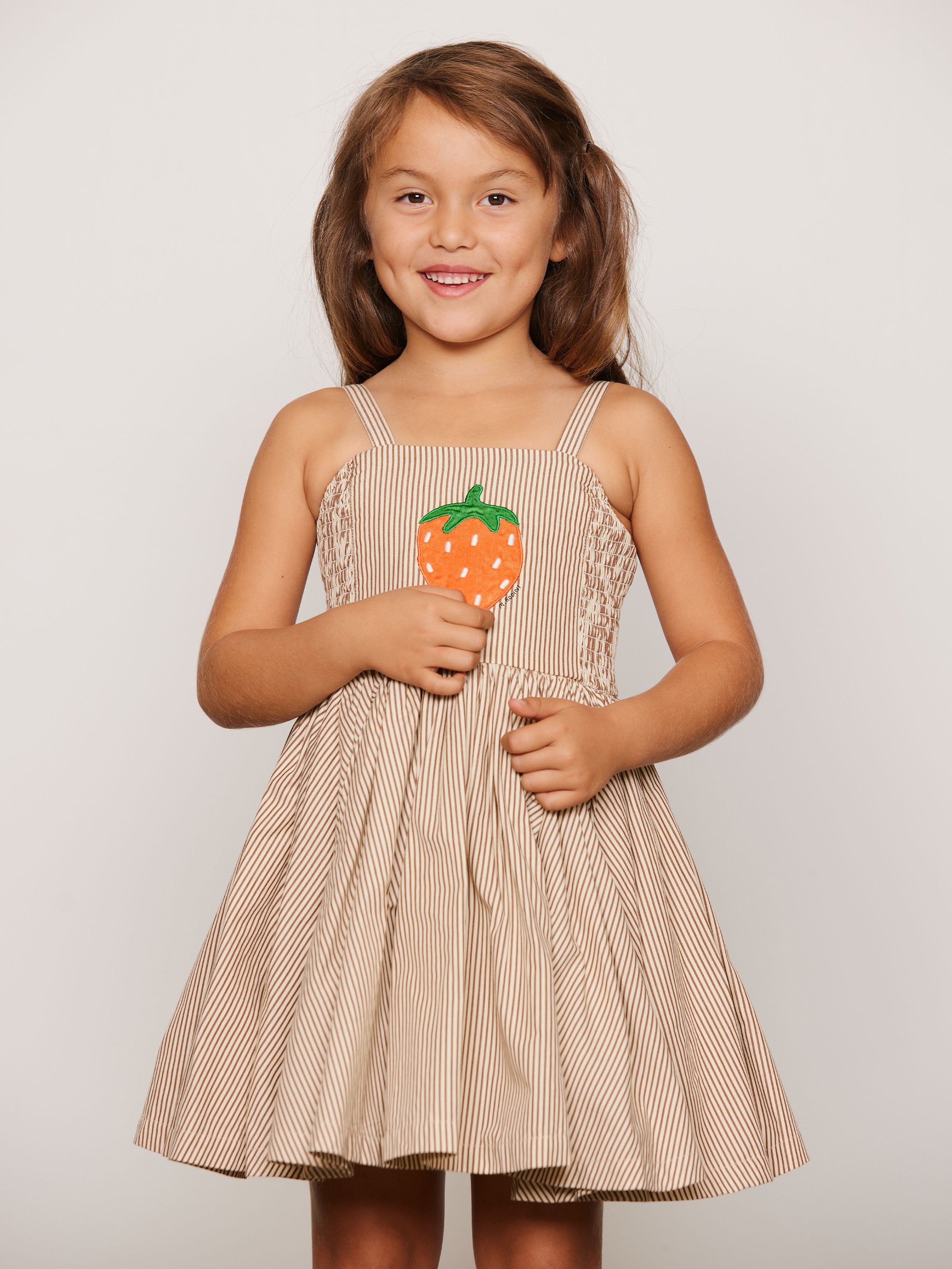Smiling child in a striped dress with a strawberry design, standing against a plain background.