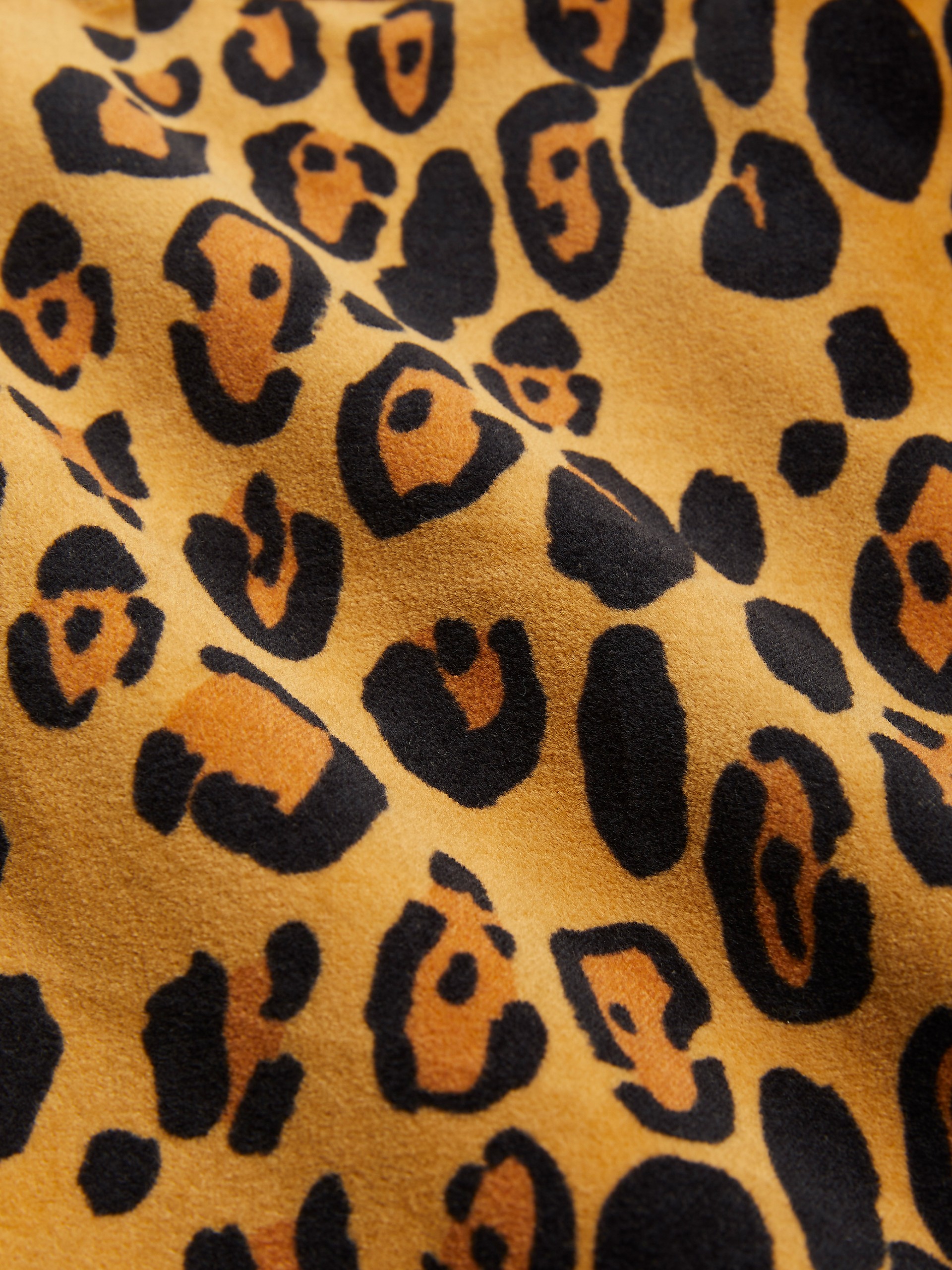 Close-up of a fabric featuring a leopard print pattern with black and orange spots on a beige background.