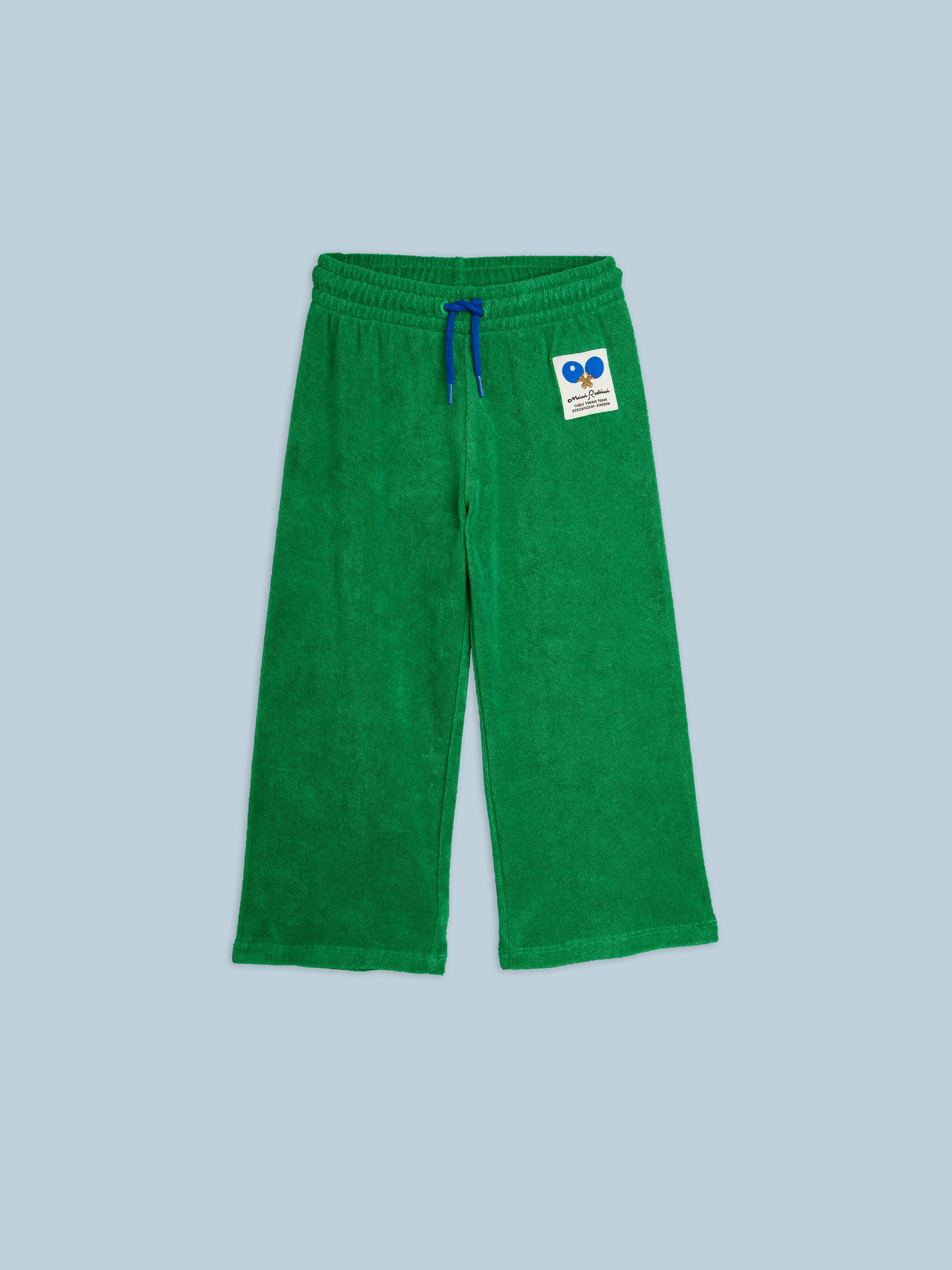 Table tennis patch terry sweatpants from Mini Rodini with an elastic waist, blue drawstring, and a logo patch featuring blue tennis rackets on the left side.
