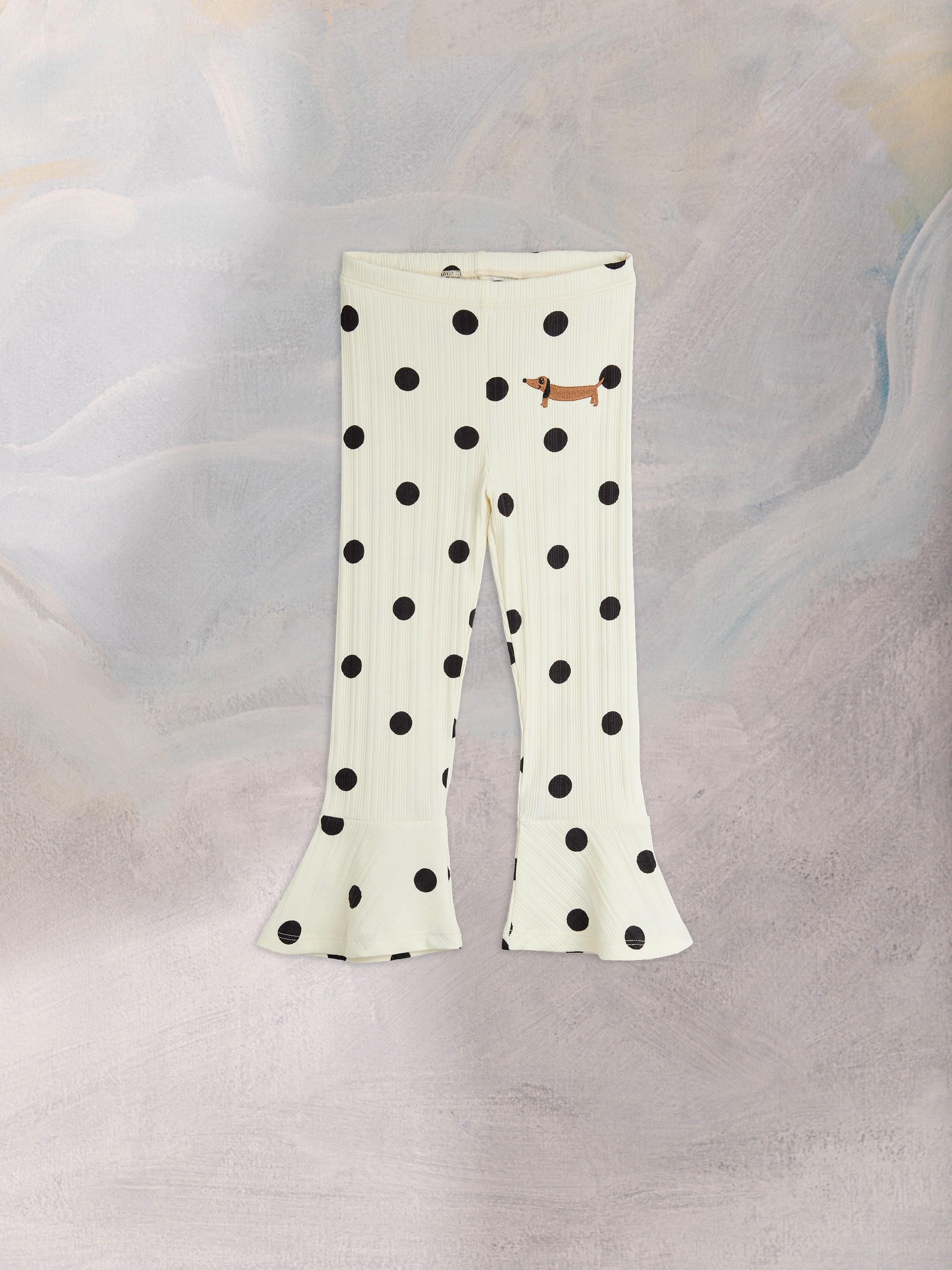 White flared pants with large black polka dots and a small brown dachshund patch on a textured gray backdrop.