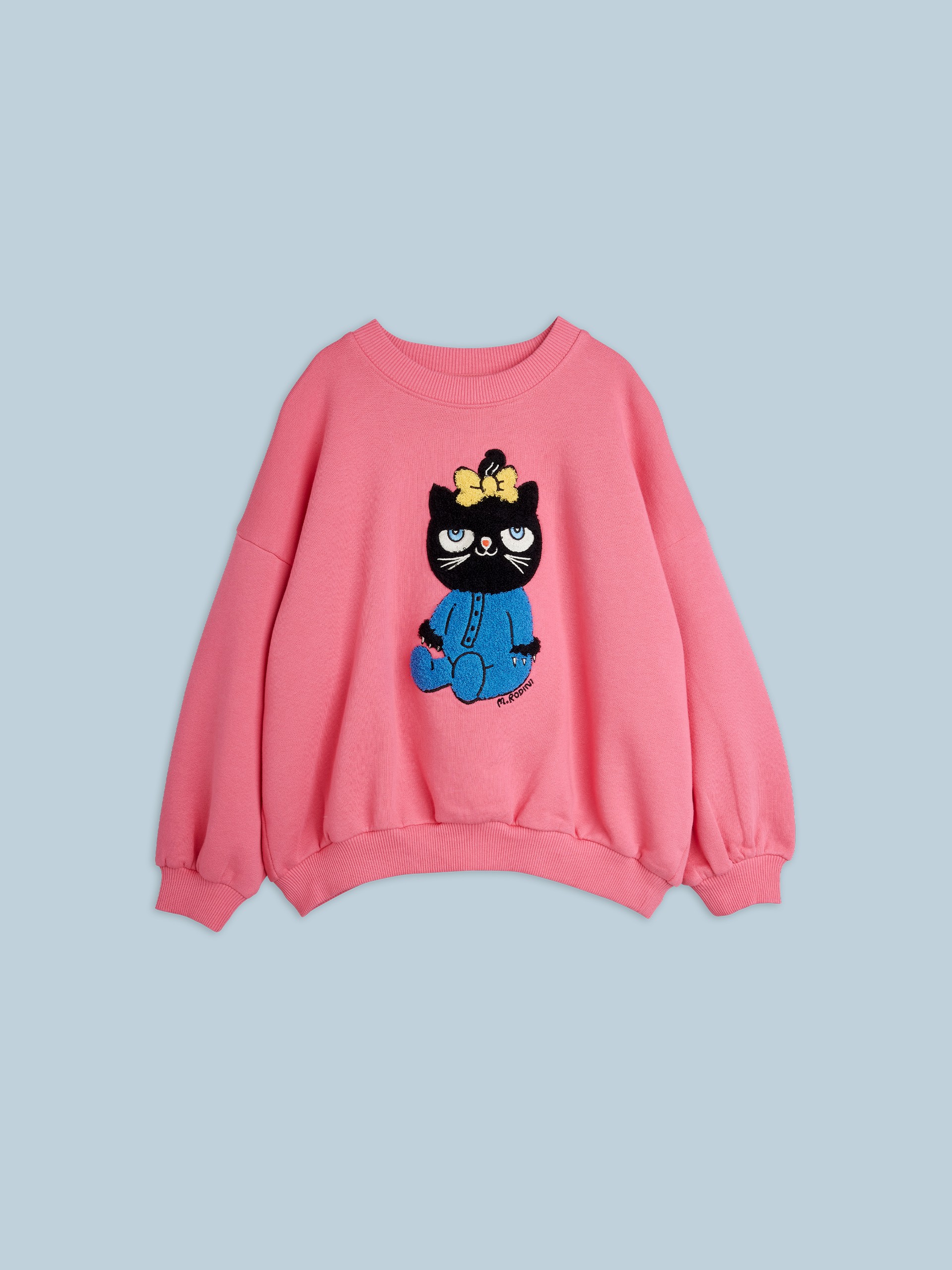 Pink sweatshirt with a black cat wearing a bow and blue overalls embroidered on the front, set against a light blue background.