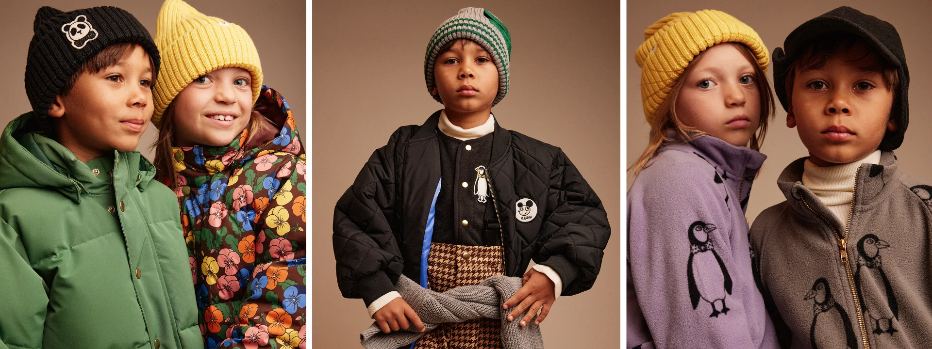 Two children in winter clothes; one wears a green jacket and black beanie, the other a floral jacket and yellow beanie, smiling softly.