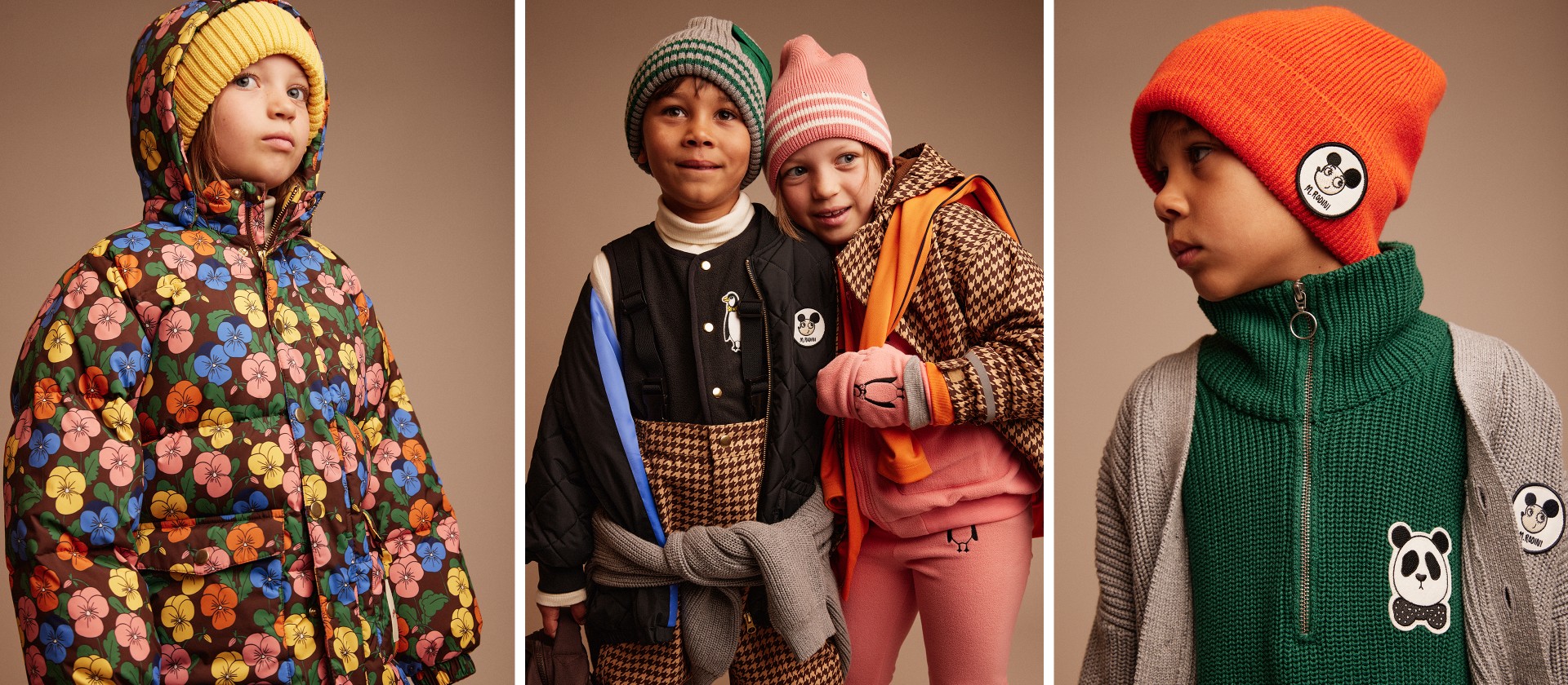 Two children in winter clothing, one in a green and grey beanie, the other in a pink beanie, both smiling and wearing patterned outfits.