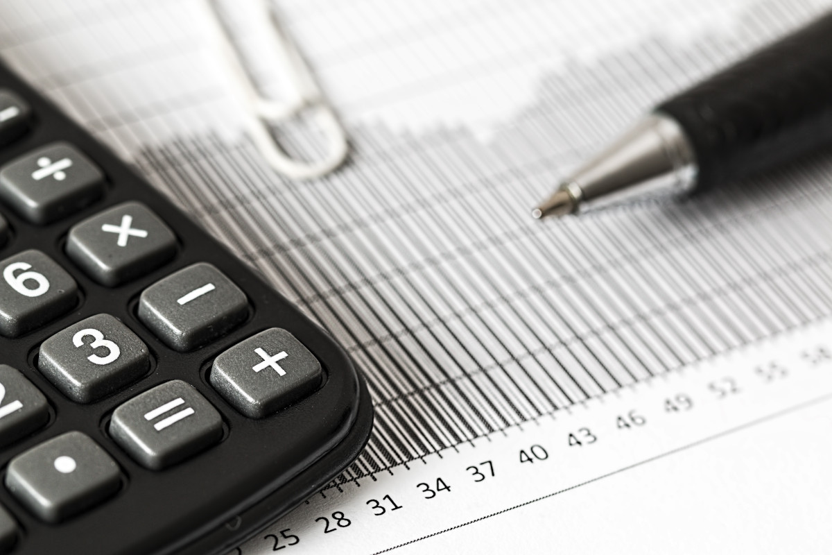 A calculator, pen, and paperclip on a financial document with a bar graph and numerical scale.