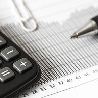 A calculator, pen, and paperclip on a financial document with a bar graph and numerical scale.