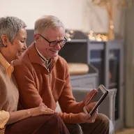 elderly couple smiling and looking at a tablet