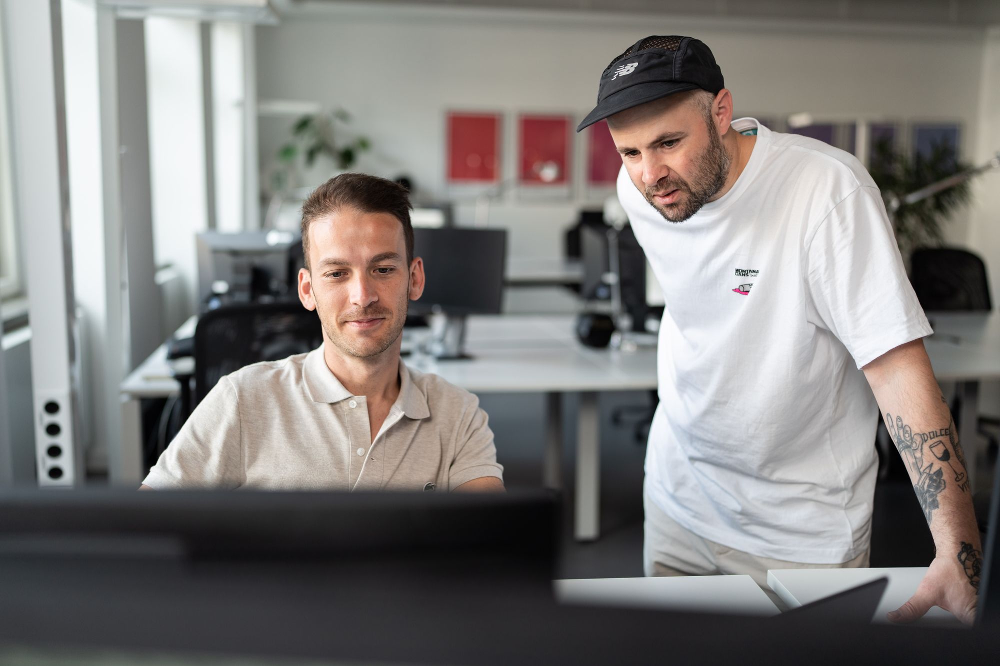 Zwei Mitarbeitende der interone München während sie sich hinter einem Monitor zu einem Projekt austauschen