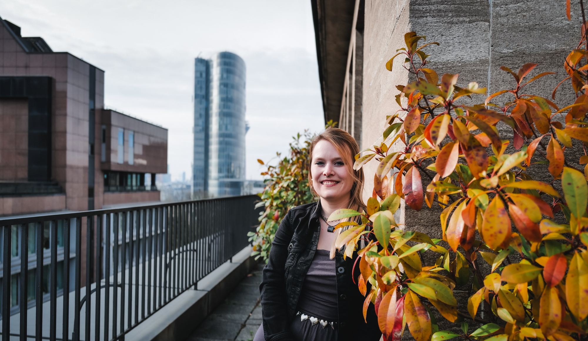 Julia auf dem Balkon im Büro Düsseldorf mit Herbstlaub; moderne Stadtlandschaft im Hintergrund