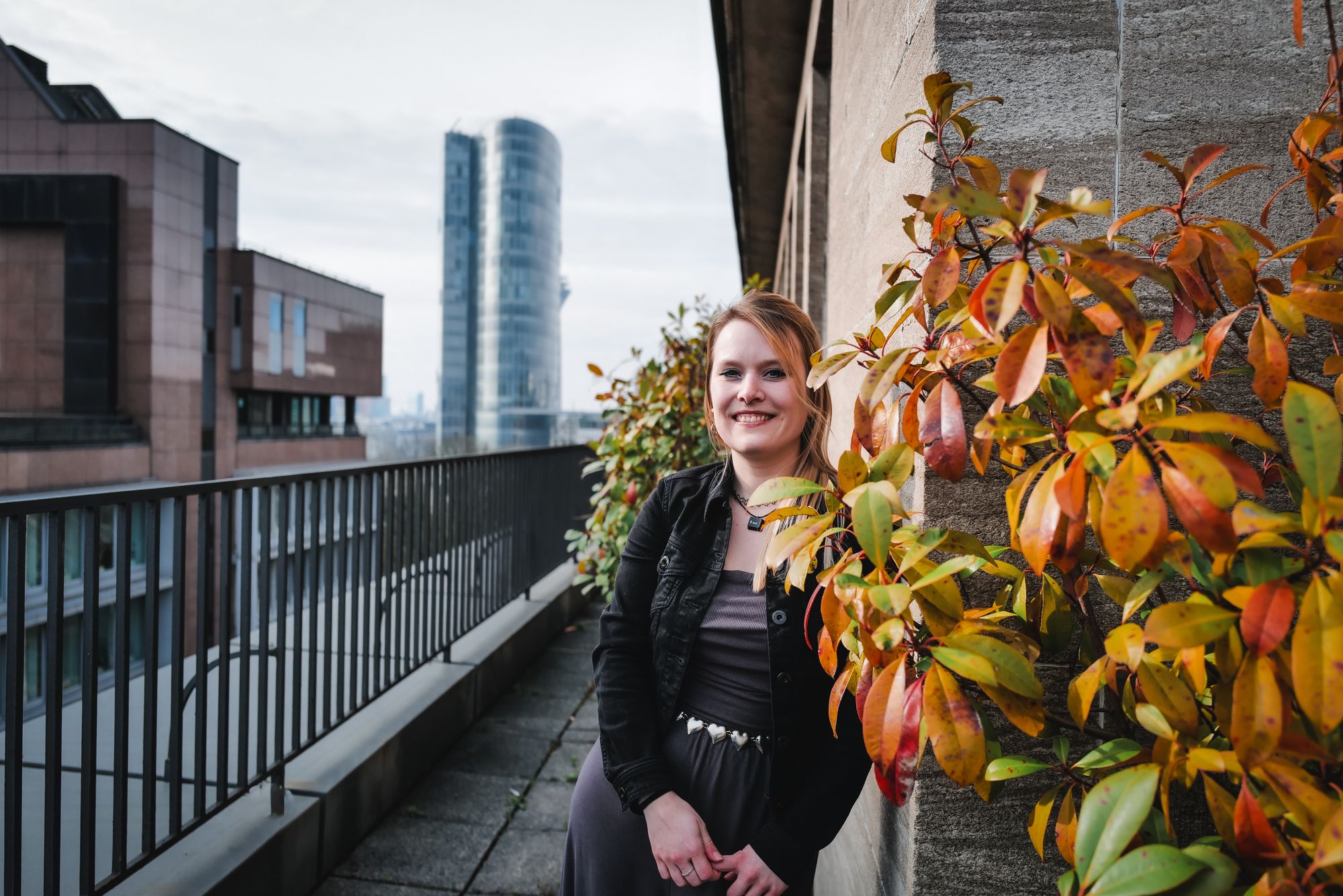 Julia auf dem Balkon im Büro Düsseldorf mit Herbstlaub; moderne Stadtlandschaft im Hintergrund