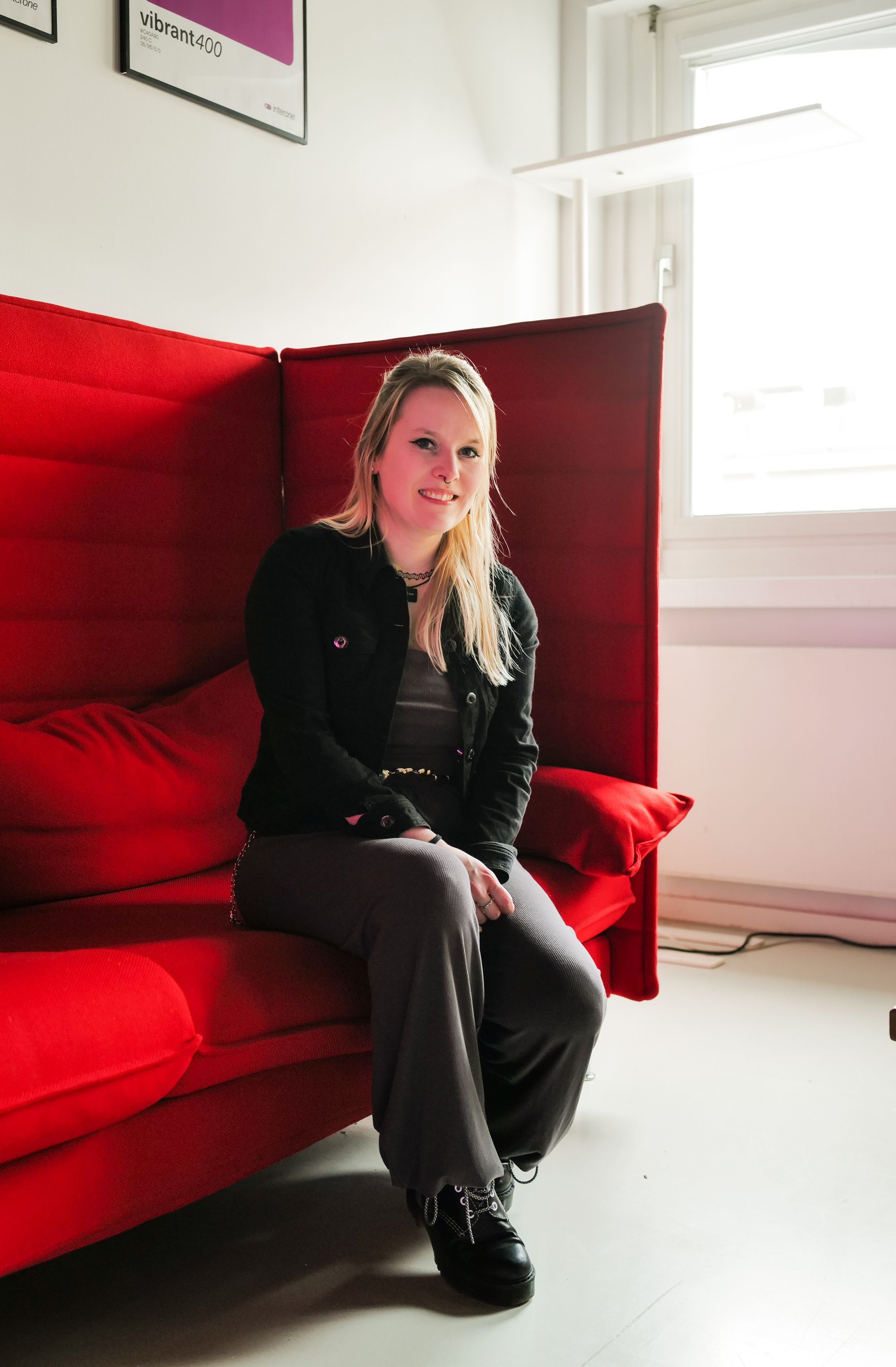 Julia sitzt auf einem roten Sofa in einem gut beleuchteten Raum mit weißen Wänden.