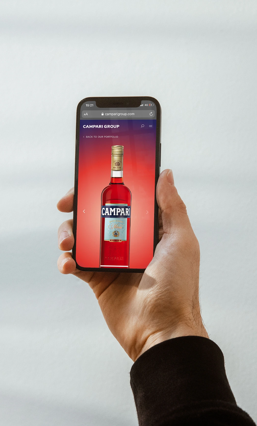 Hand holding a smartphone displaying a Campari bottle on a red background, with the Campari Group website open.
