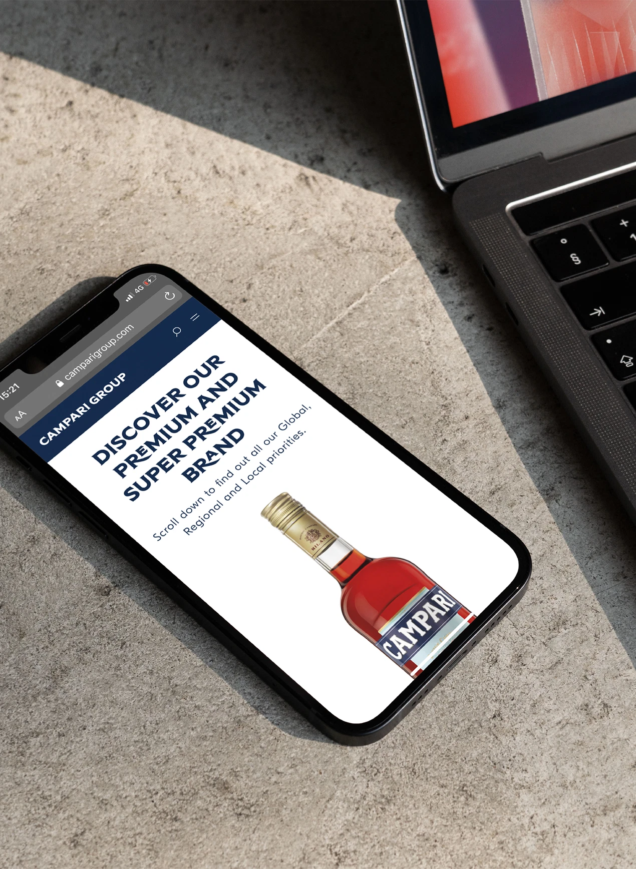 Smartphone displaying a Campari Group promotion next to a laptop on a stone surface.