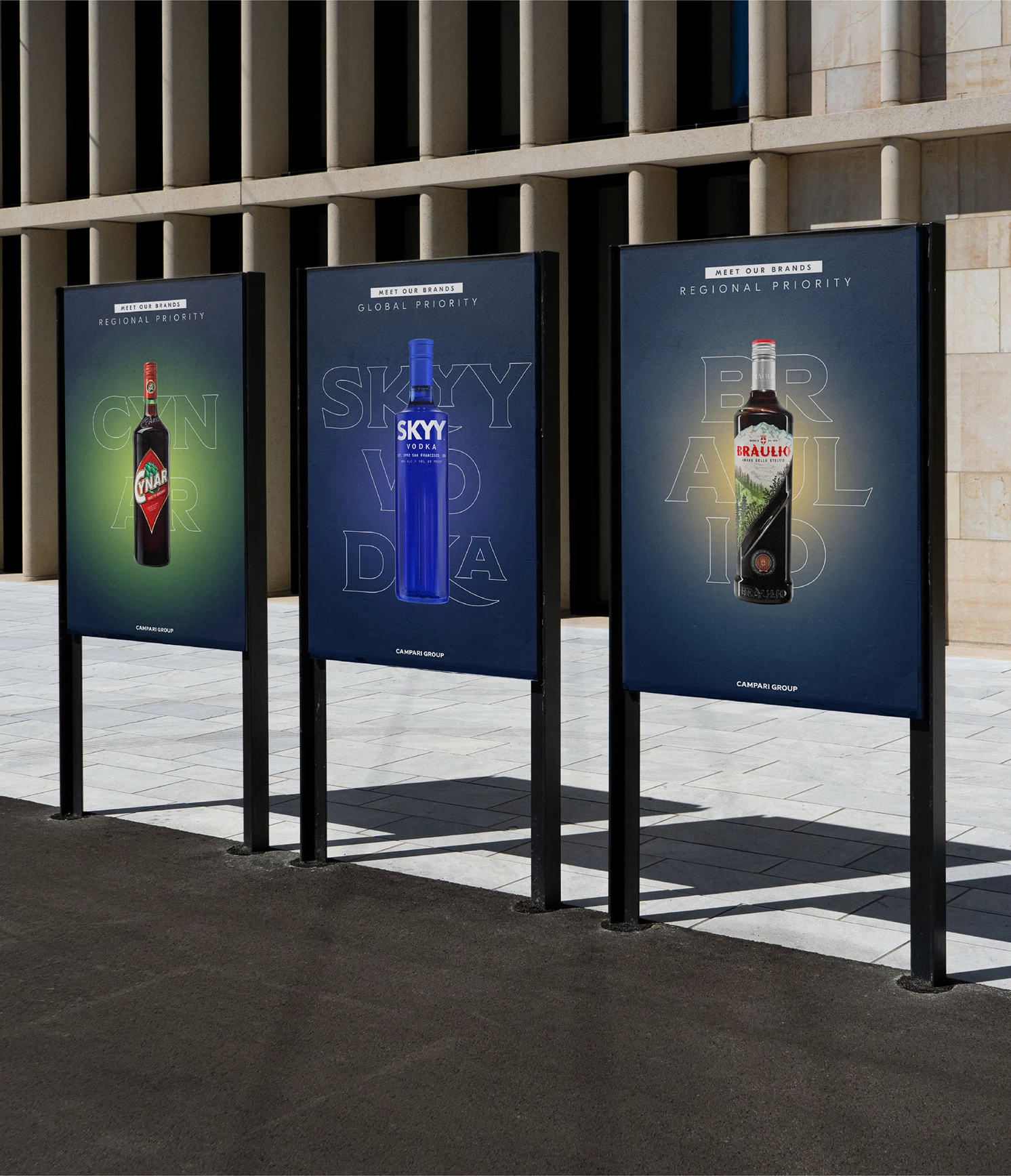 Three outdoor posters display various liquor brands against a modern building facade.