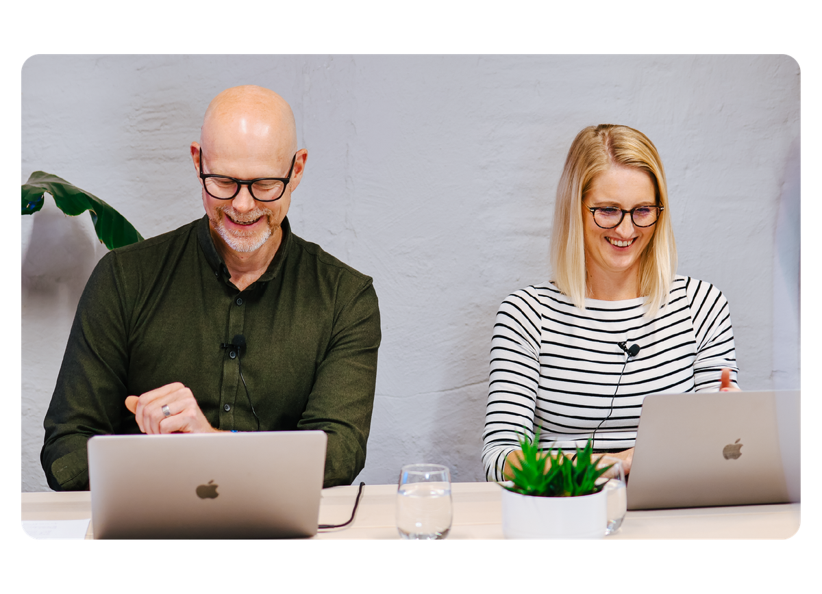 Två glada personer sitter bredvid varandra och arbetar
