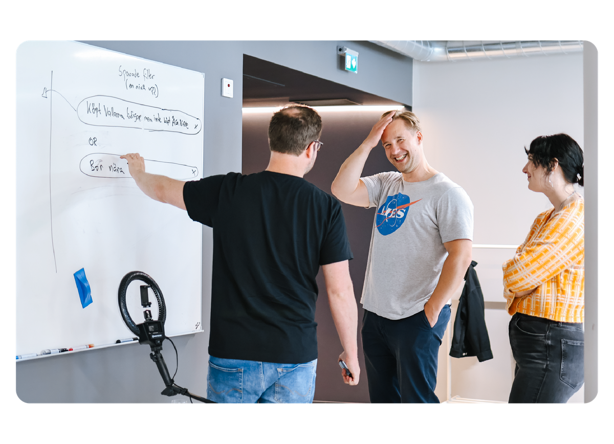 Tre personer står vid en whiteboard och diskuterar ett arbetsprojekt