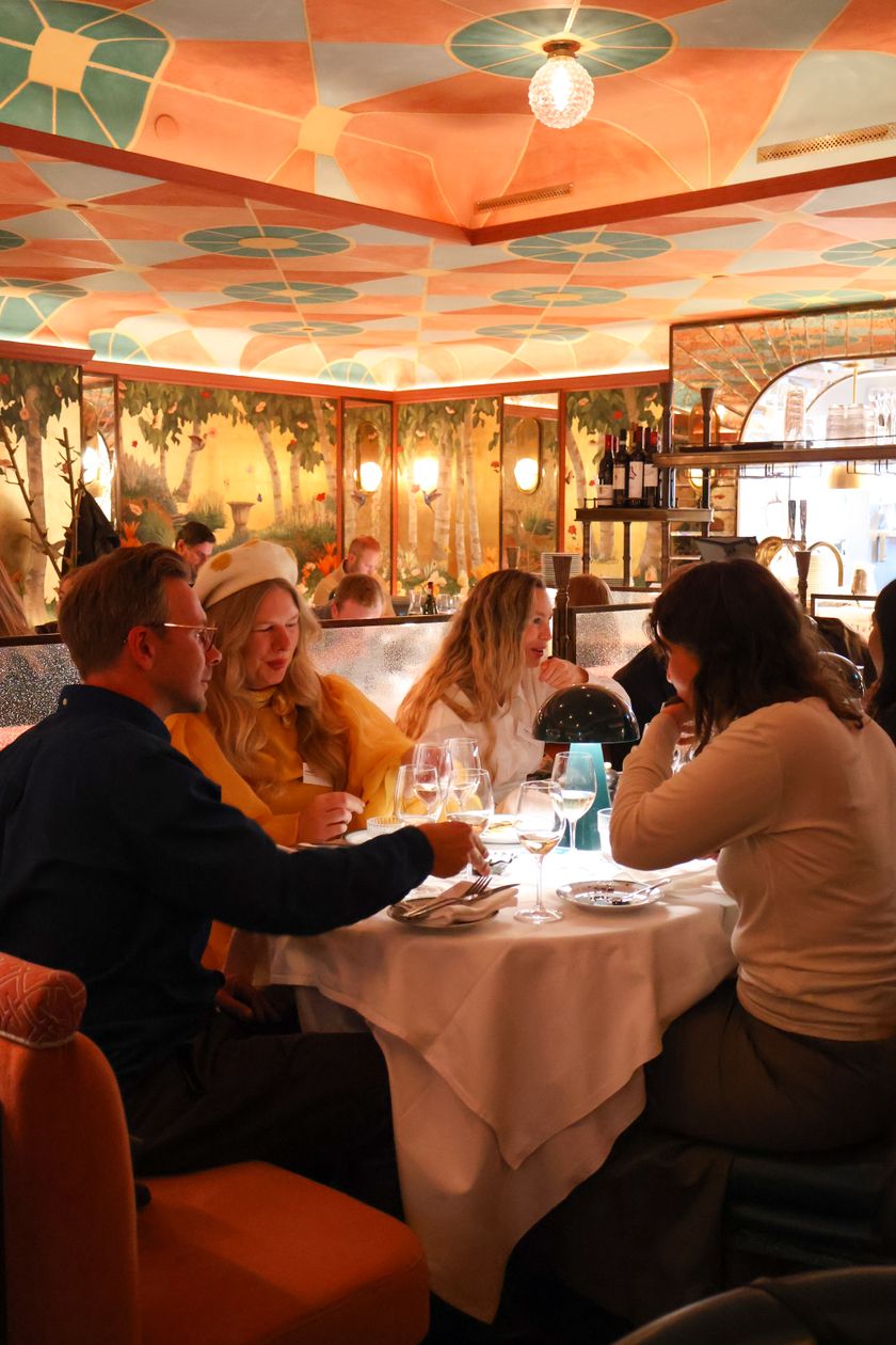 Four people having dinner at an elegantly decorated restaurant with an orange-patterned ceiling, murals, and warm, mood lighting.