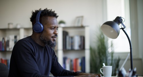A man sitting at a desk typing on a laptop while wearing headphones