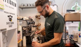A barista pouring frothed milk into a resuable coffee cup