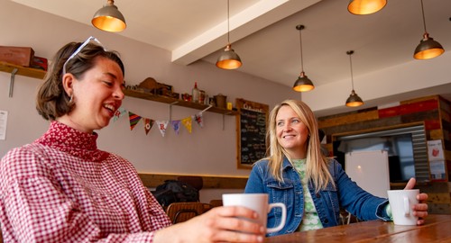 Two women sitting at a wooden table having a conversation and a cup of coffee