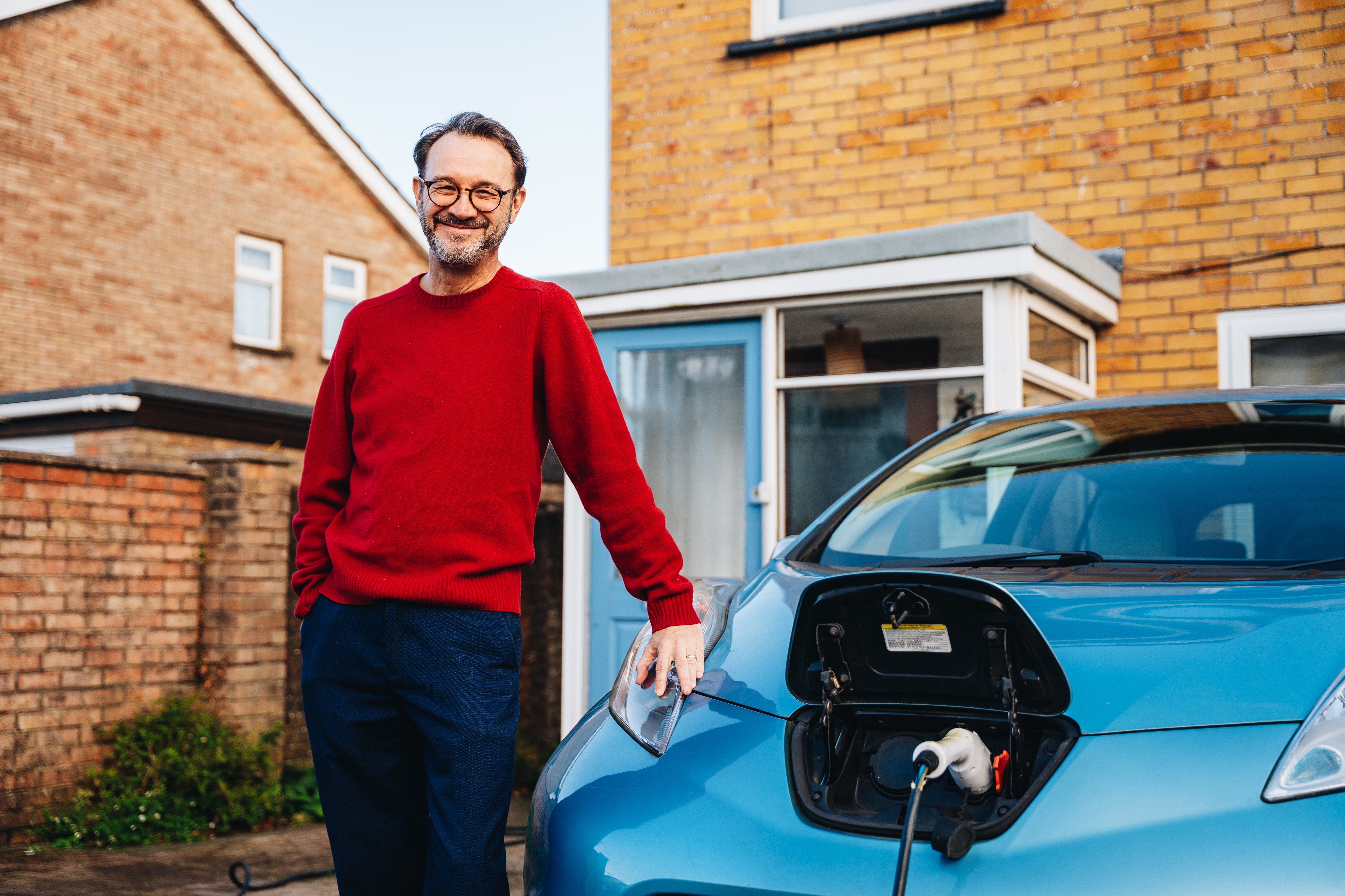 A man stood next to an electric vehicle that's plugged in to charge