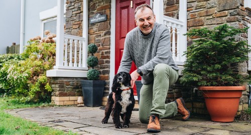 A man outside his front door kneeling next to his black and white dog