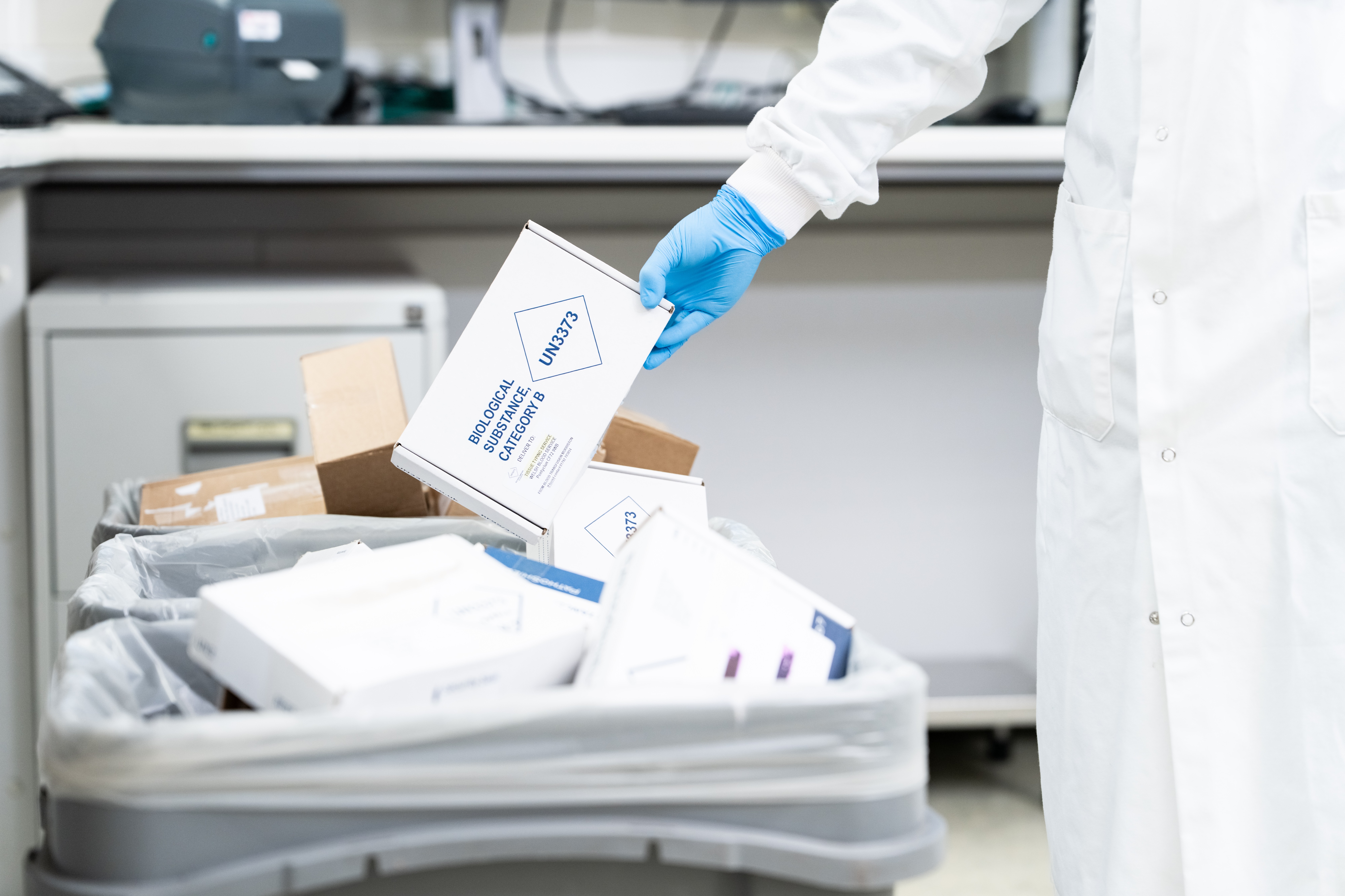 A hand holding a cardboard box over a recycling bin