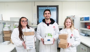 Three people holding boxes standing in a lab