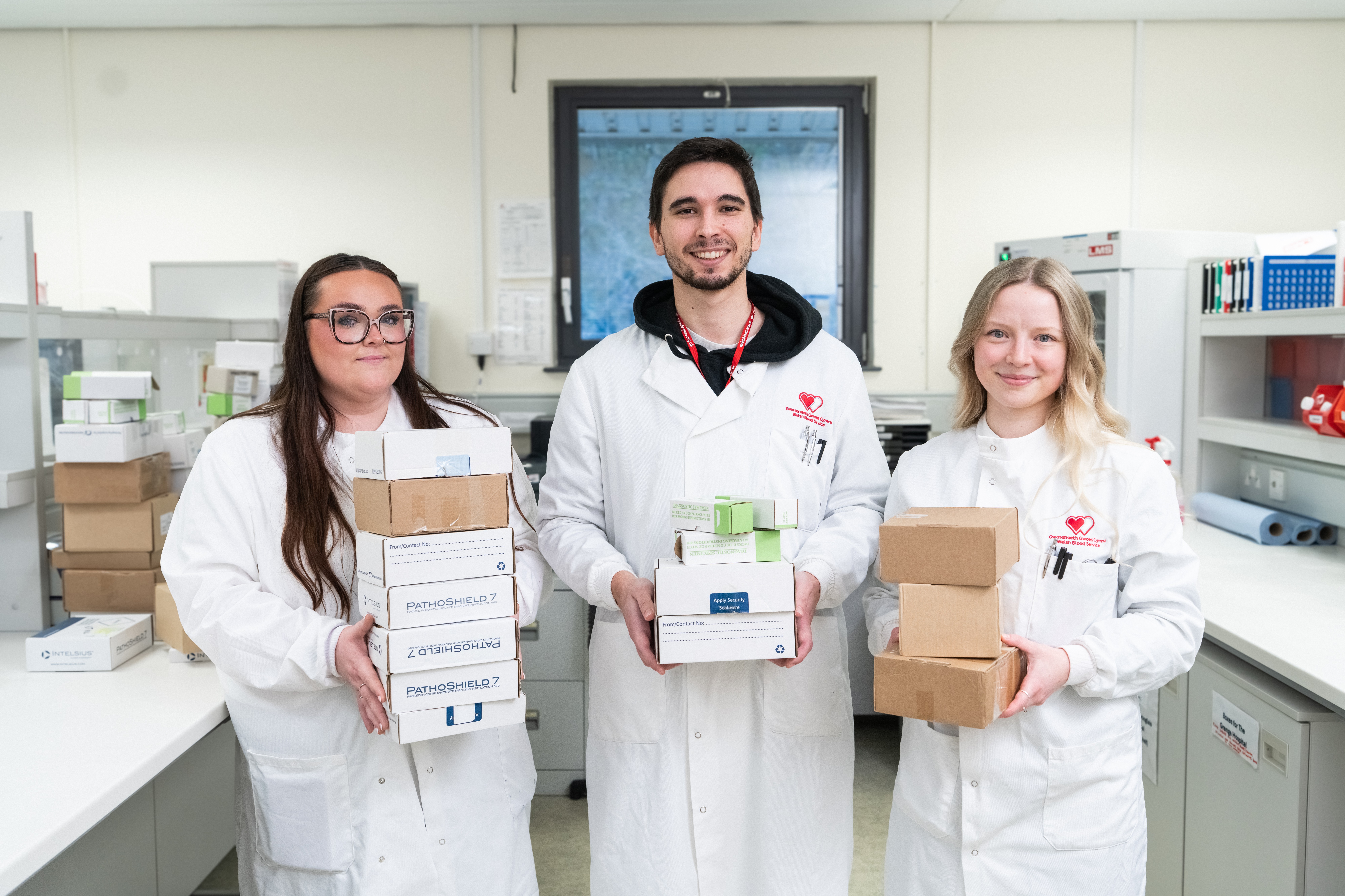 Three people holding boxes standing in a lab