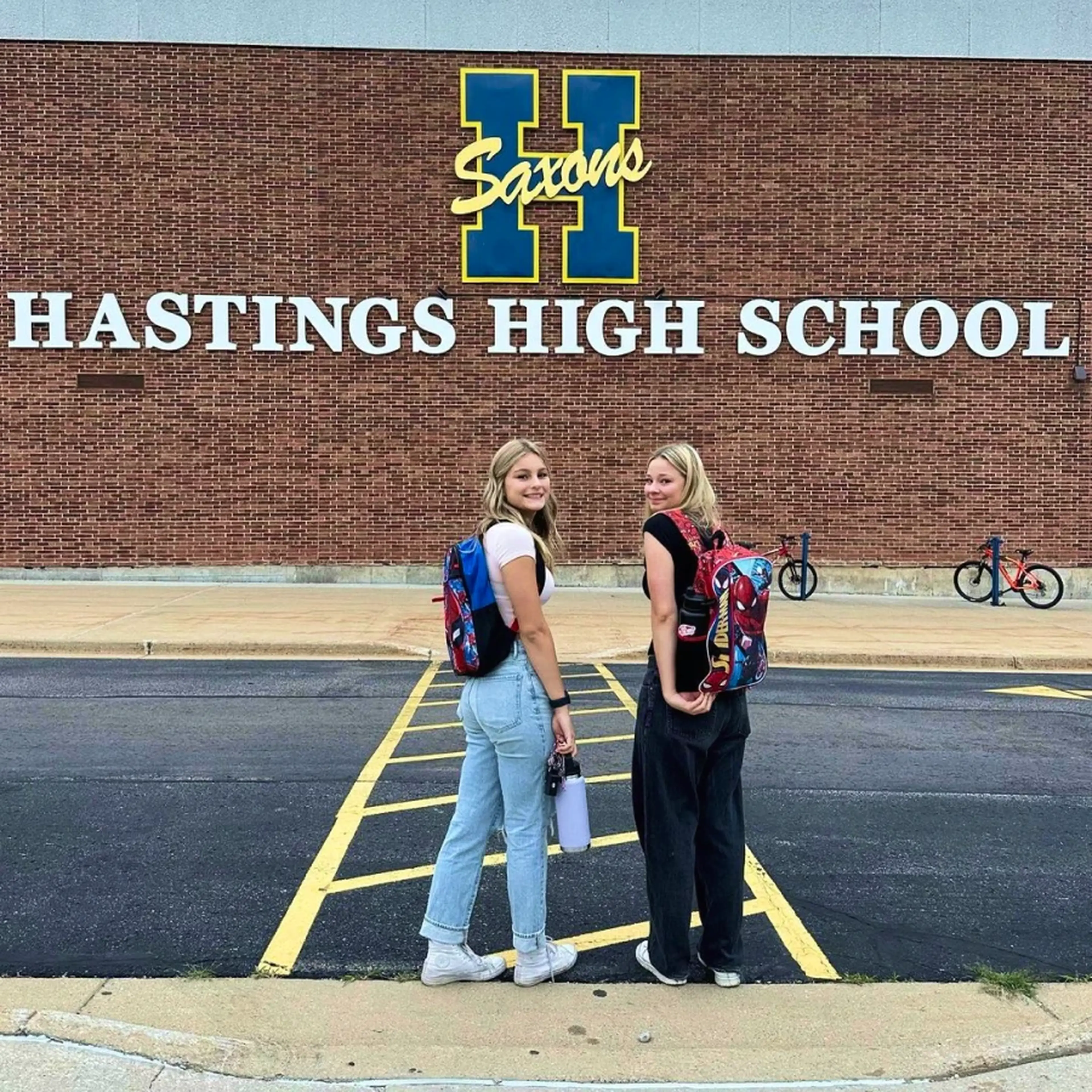 Two students with backpacks stand outside Hastings High School, smiling at the camera.