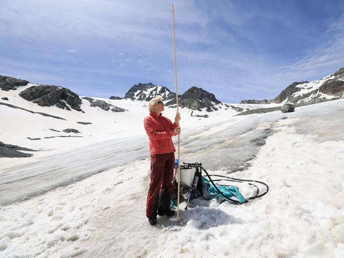 Glaziologin Andrea Fischer mit einem langem Messstab auf einem Gletscher..